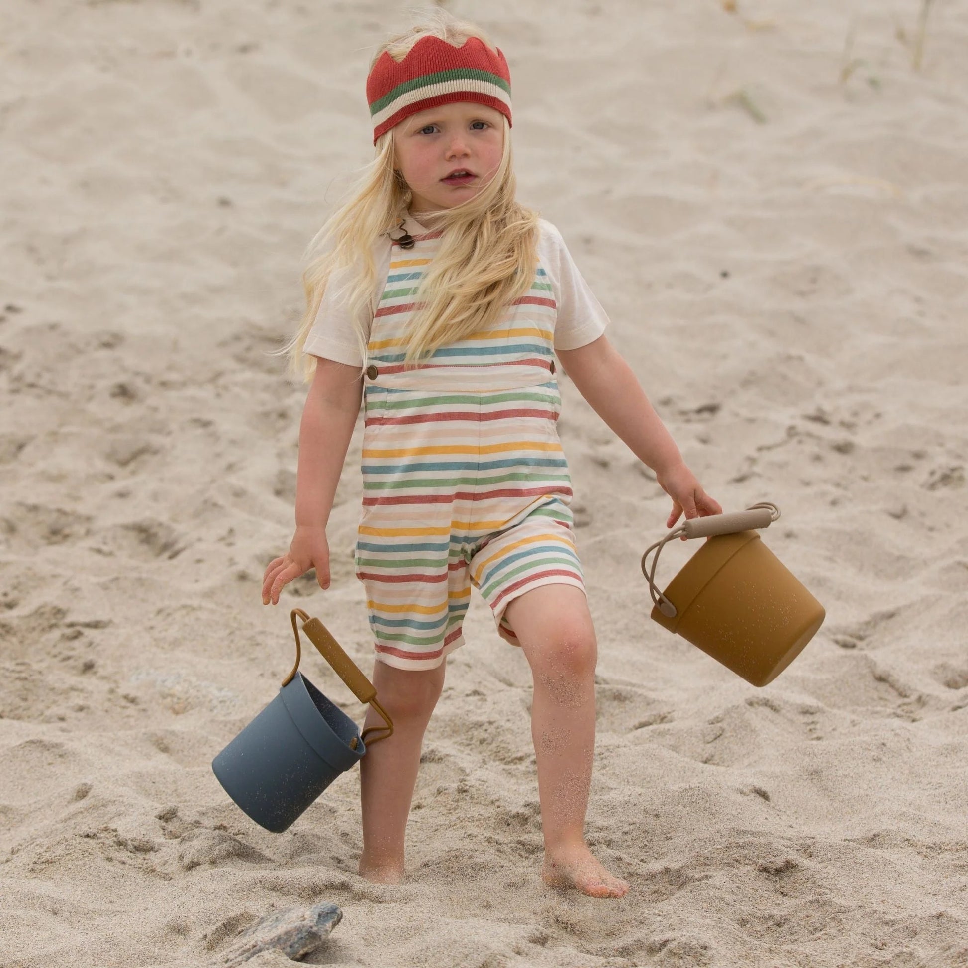 a child playing on the beach wearing striped overall shorts