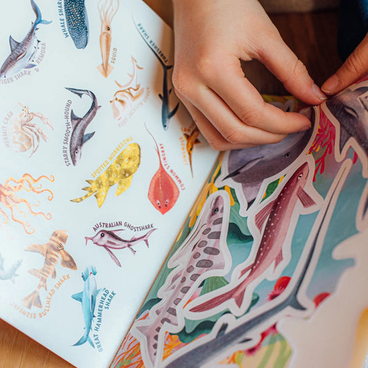 A hand peeling off a sticker from a sharks & friends sticker book