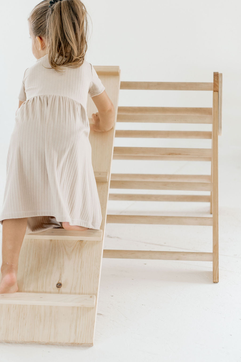 Child in a white dress standing on a wooden step stool with a ladder