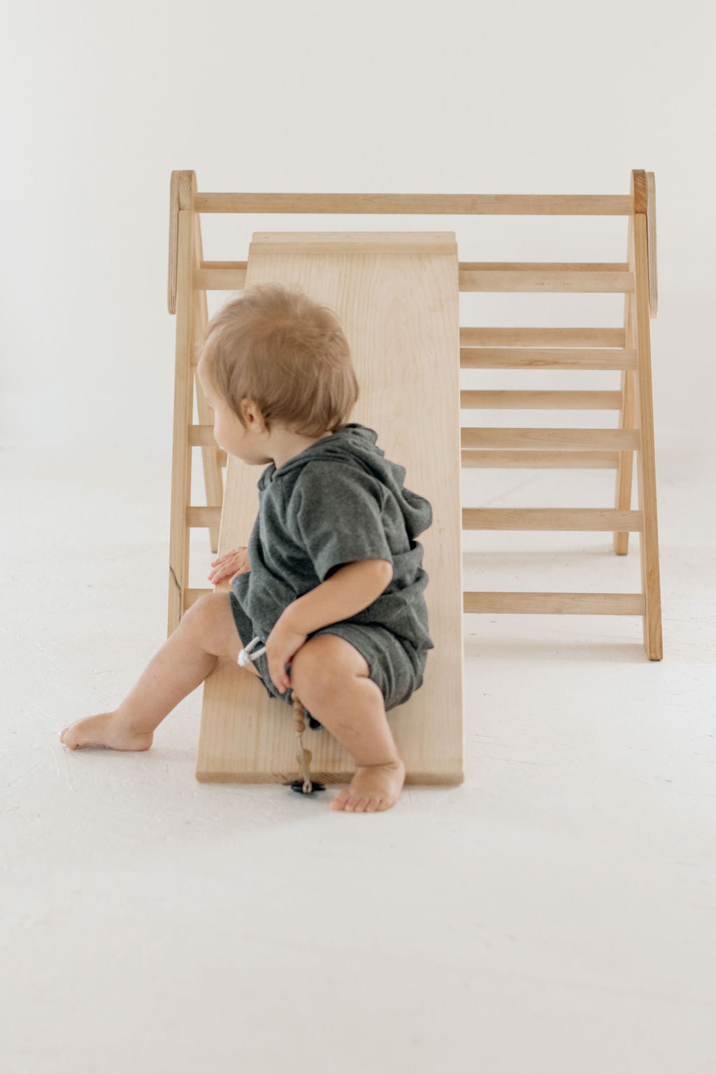 Child playing with a wooden climbing toy on a white background