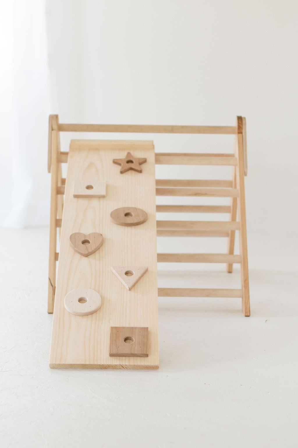 Wooden climbing toy with various shapes on a white background