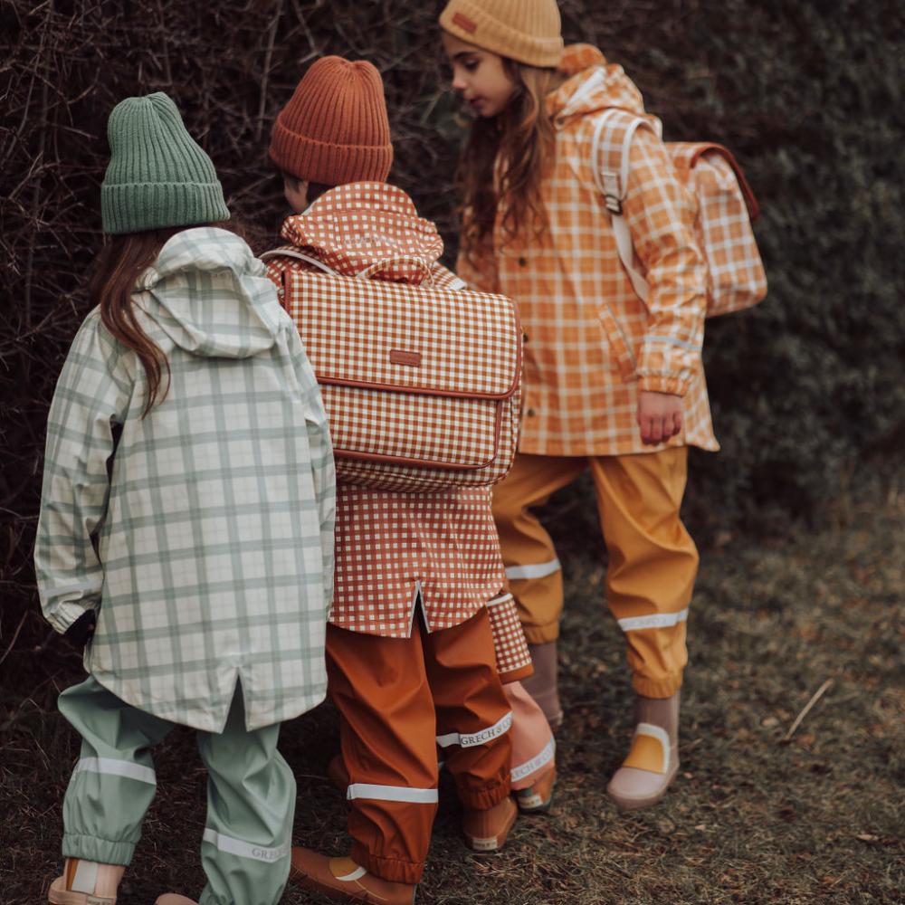 Three children in colorful raincoats and hats standing in a forest.