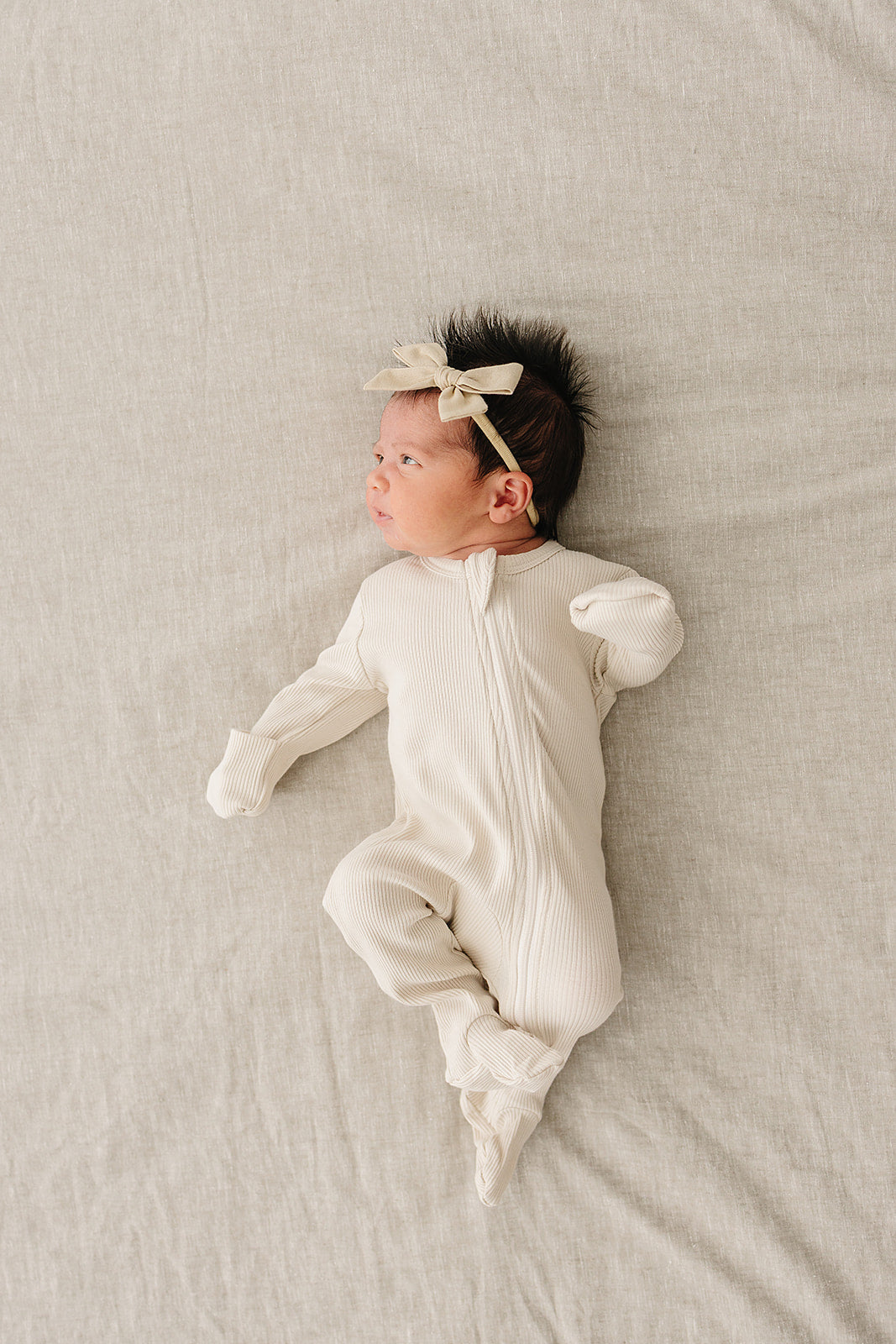 Newborn baby in a white onesie with a bow on a beige blanket