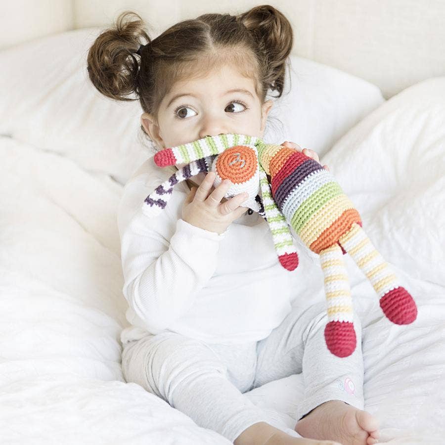 Child holding a colorful striped toy on a white bed
