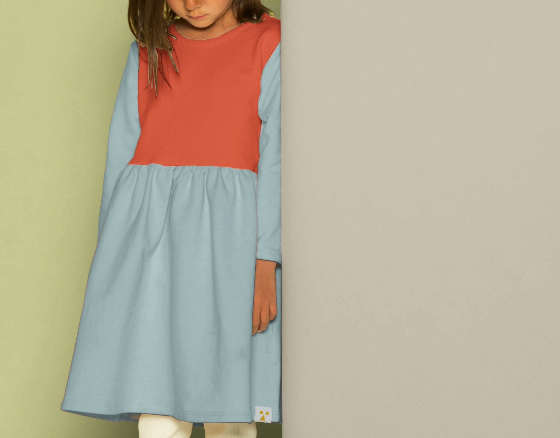 Child wearing a red and blue dress against a beige wall