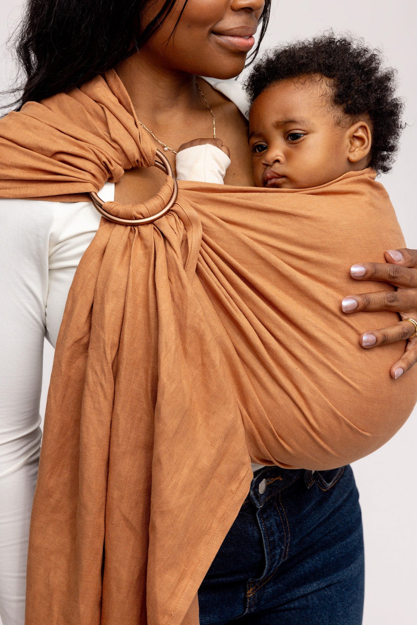 Woman holding a baby in a brown sling against a plain background