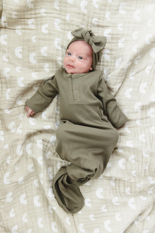 Baby in a green outfit lying on a textured white blanket
