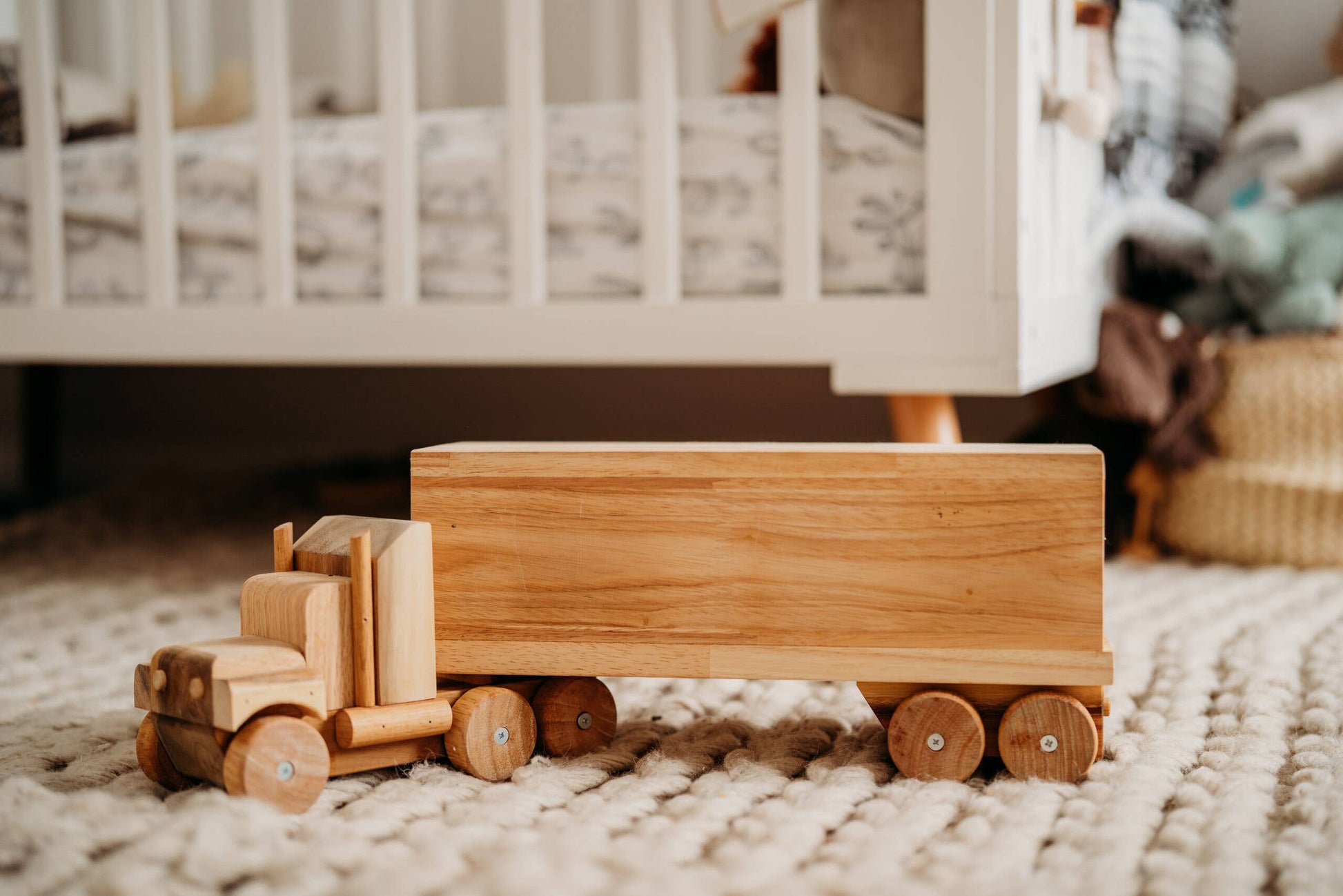 Wooden toy truck on a textured surface with a crib in the background