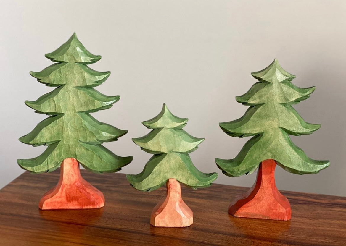 Three wooden Christmas tree figurines on a wooden surface with a plain background
