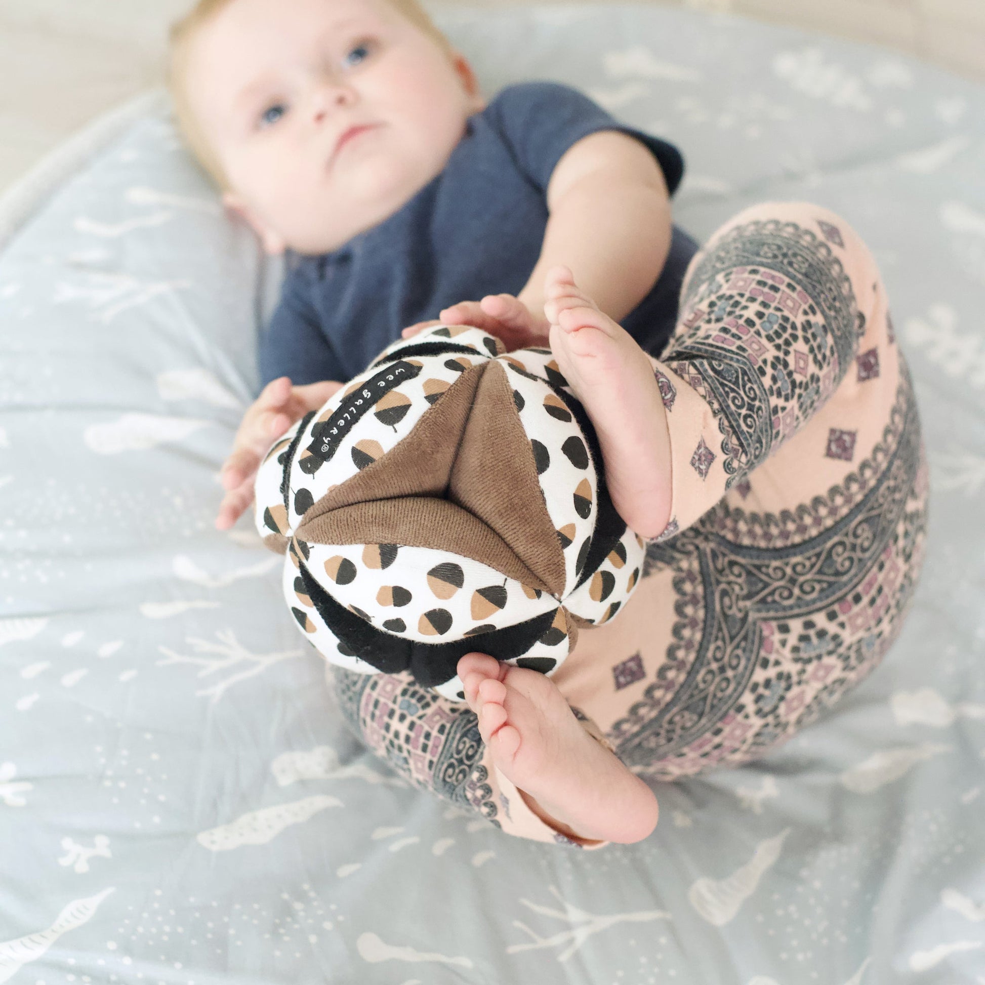 Baby playing with a patterned ball on a light blue blanket