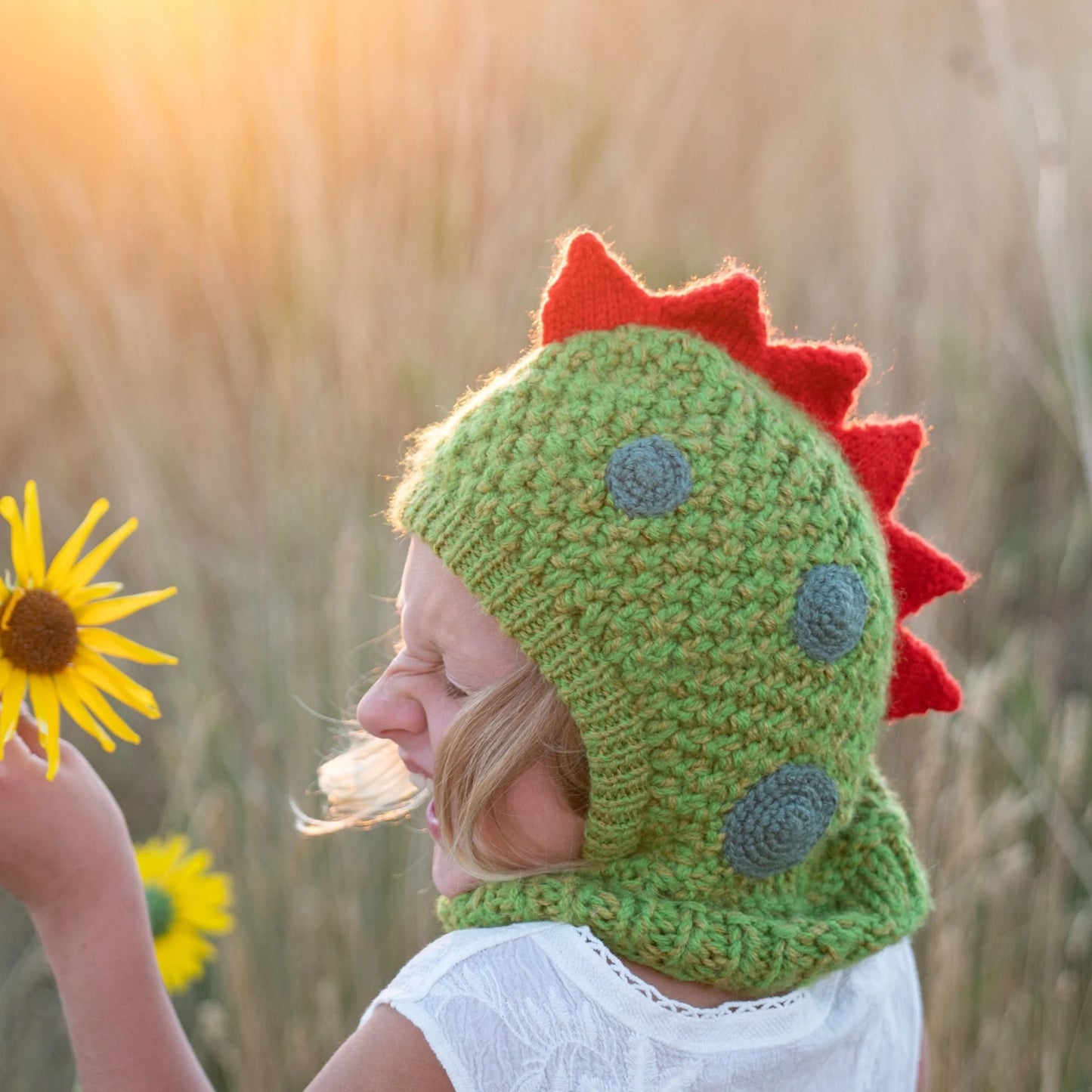 Child holding a sunflower in a case wearing wool dinosaur hood