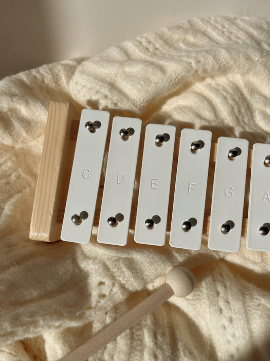 Wooden xylophone with white keys on a textured beige surface
