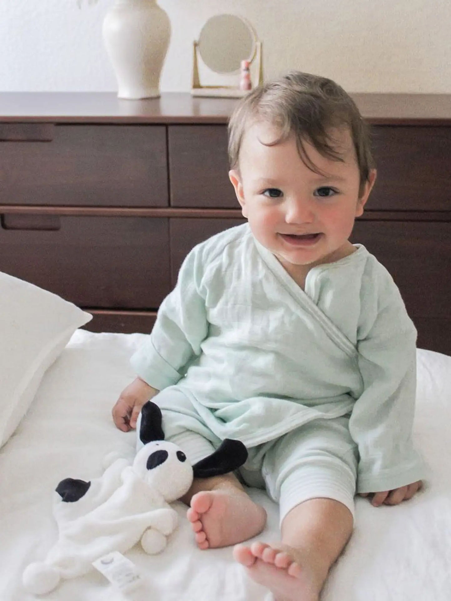 baby sitting on a bed in the Muslin Side Snap Sea Wrap Kimono by under the nile