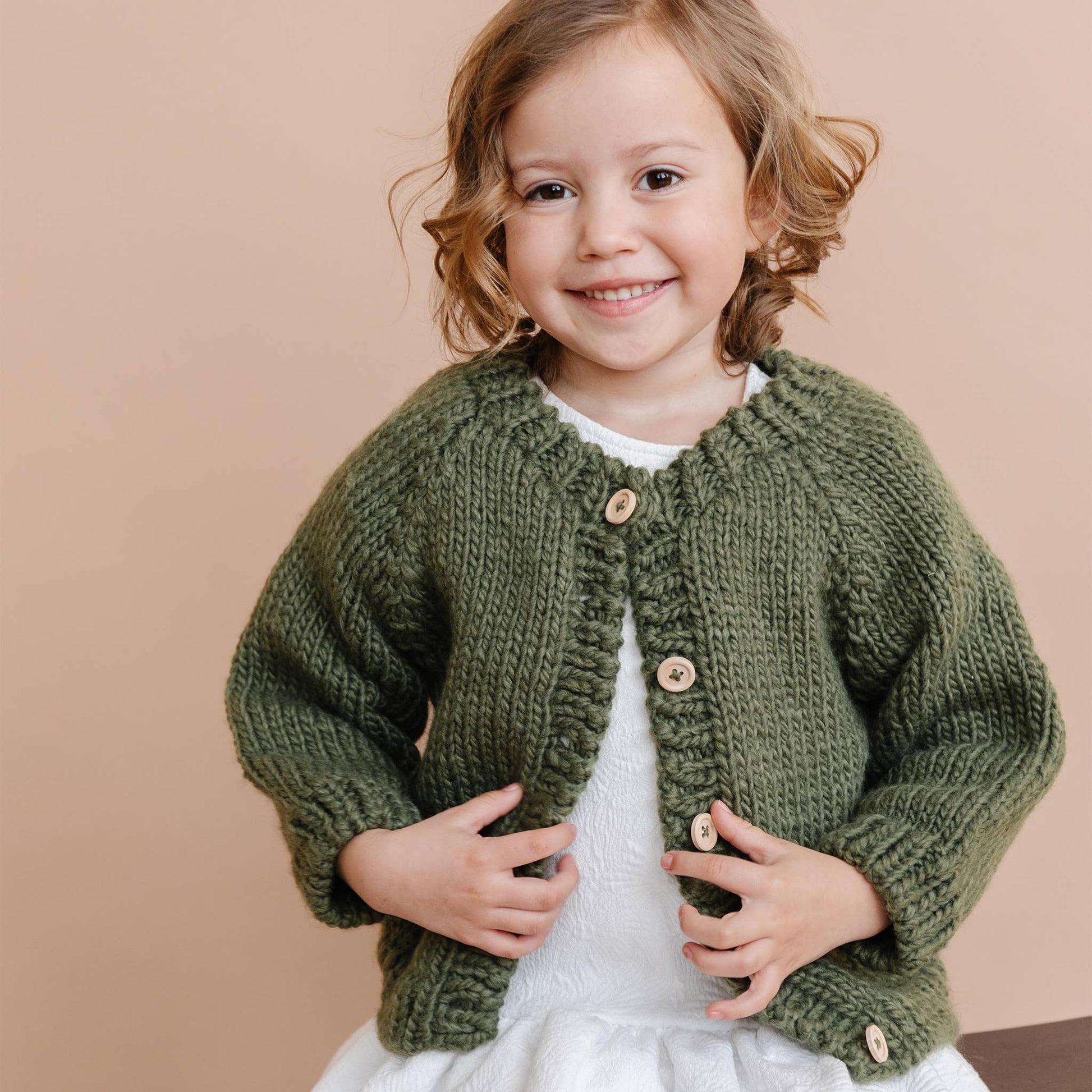 Child wearing a green knitted cardigan against a beige background
