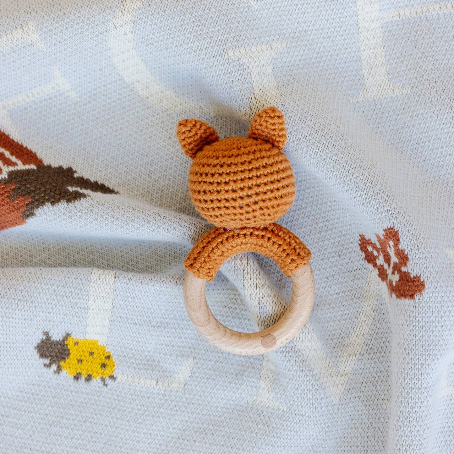 Crocheted fox teething ring with wooden base on a patterned fabric background