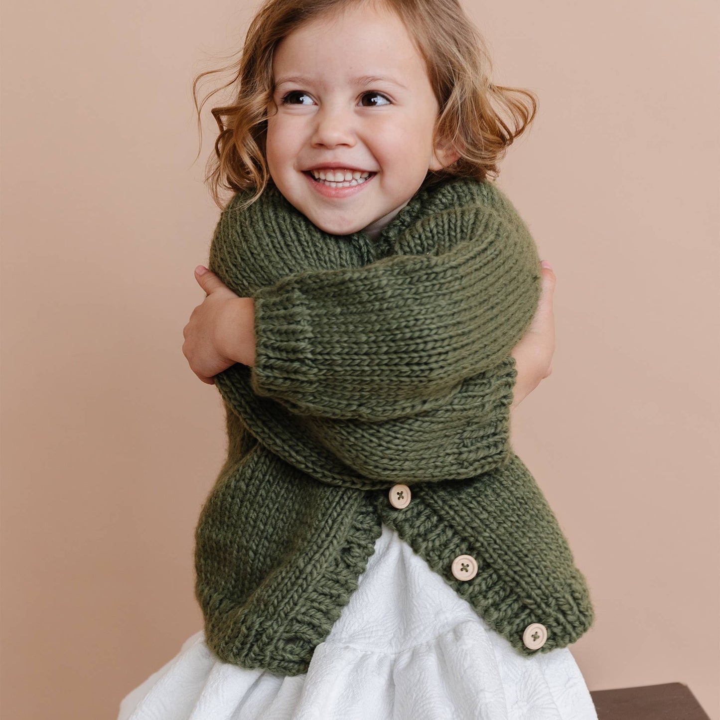 Child wearing a green knitted cardigan with buttons against a beige background
