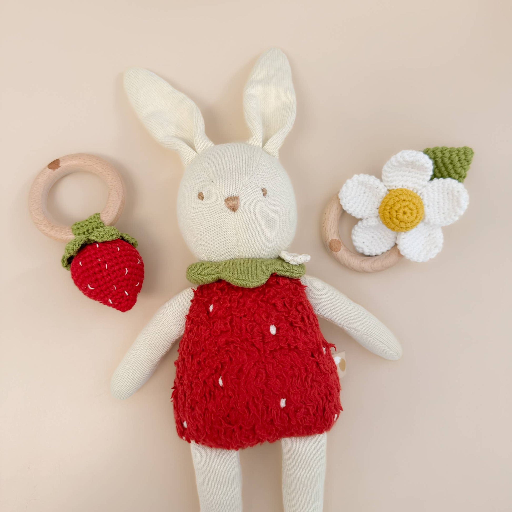 Knitted bunny toy in a red dress with a strawberry ring and flower on a beige background