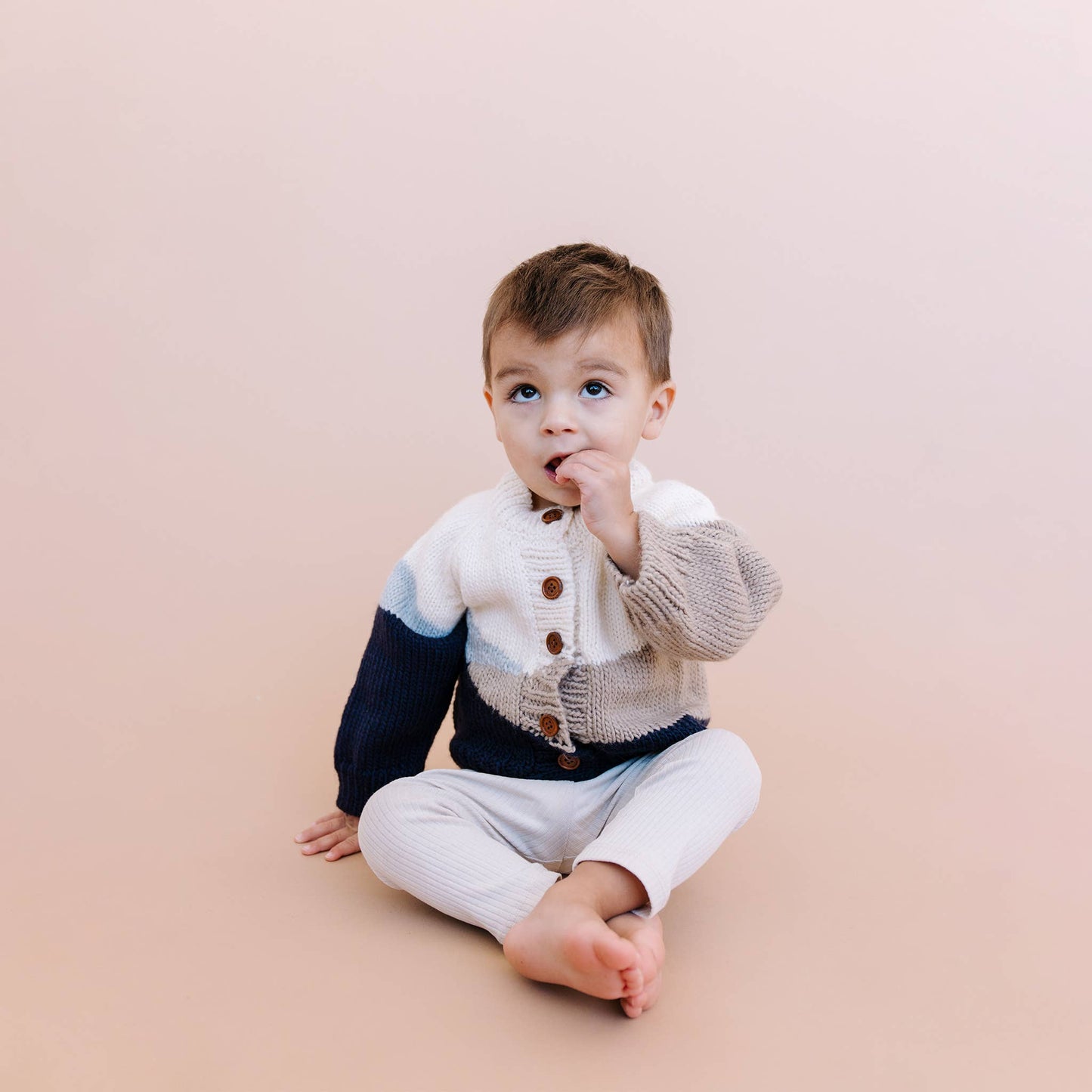Child wearing a sunset cardigan and white pants on a beige background