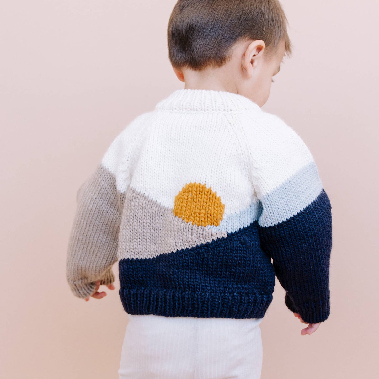 Child wearing a colorful knit sweater with a sun design on a plain background