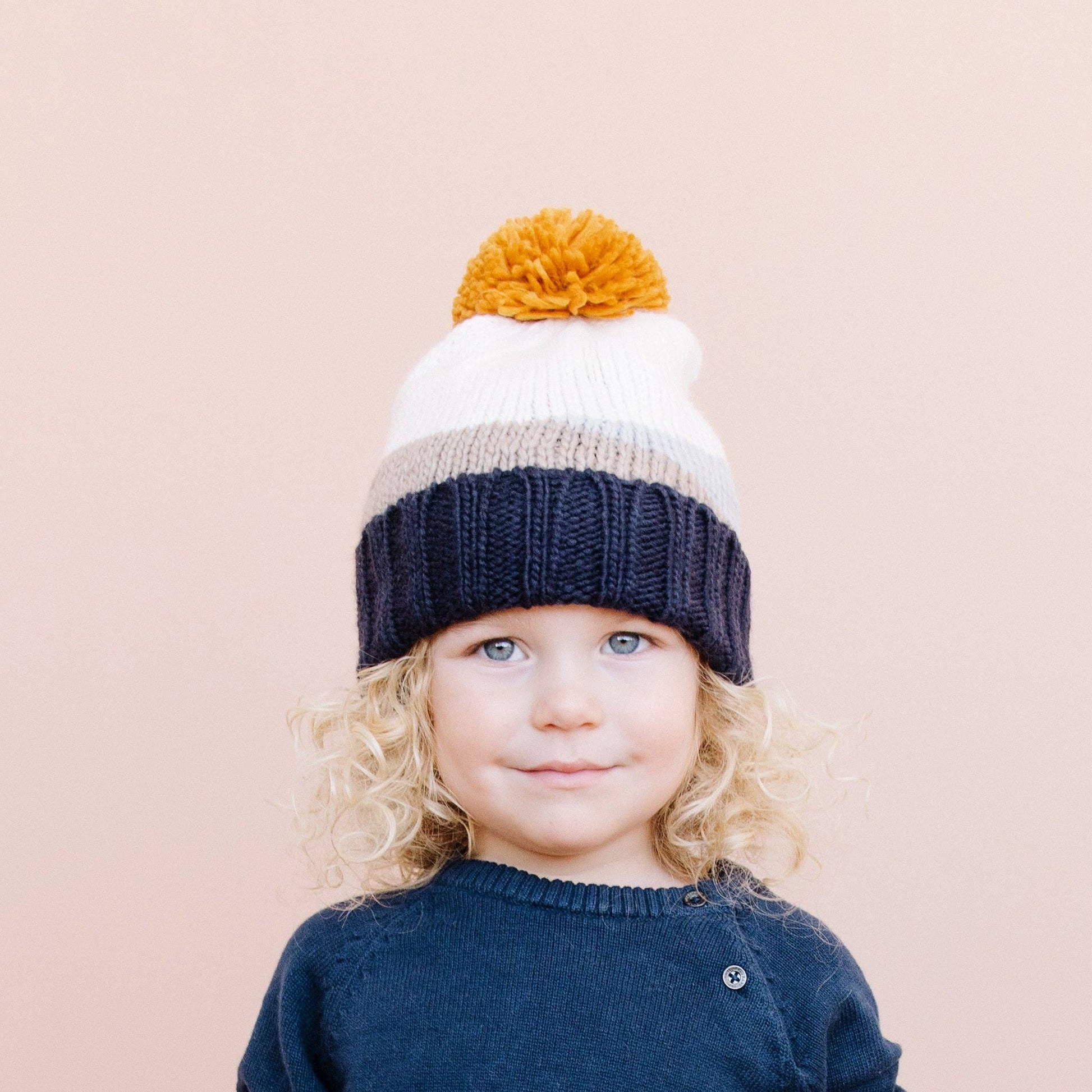 Child wearing a colorful knit hat with a pom-pom on a beige background