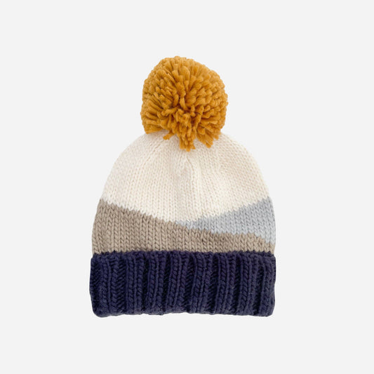 Knitted hat with a mustard yellow pom-pom on a light gray background