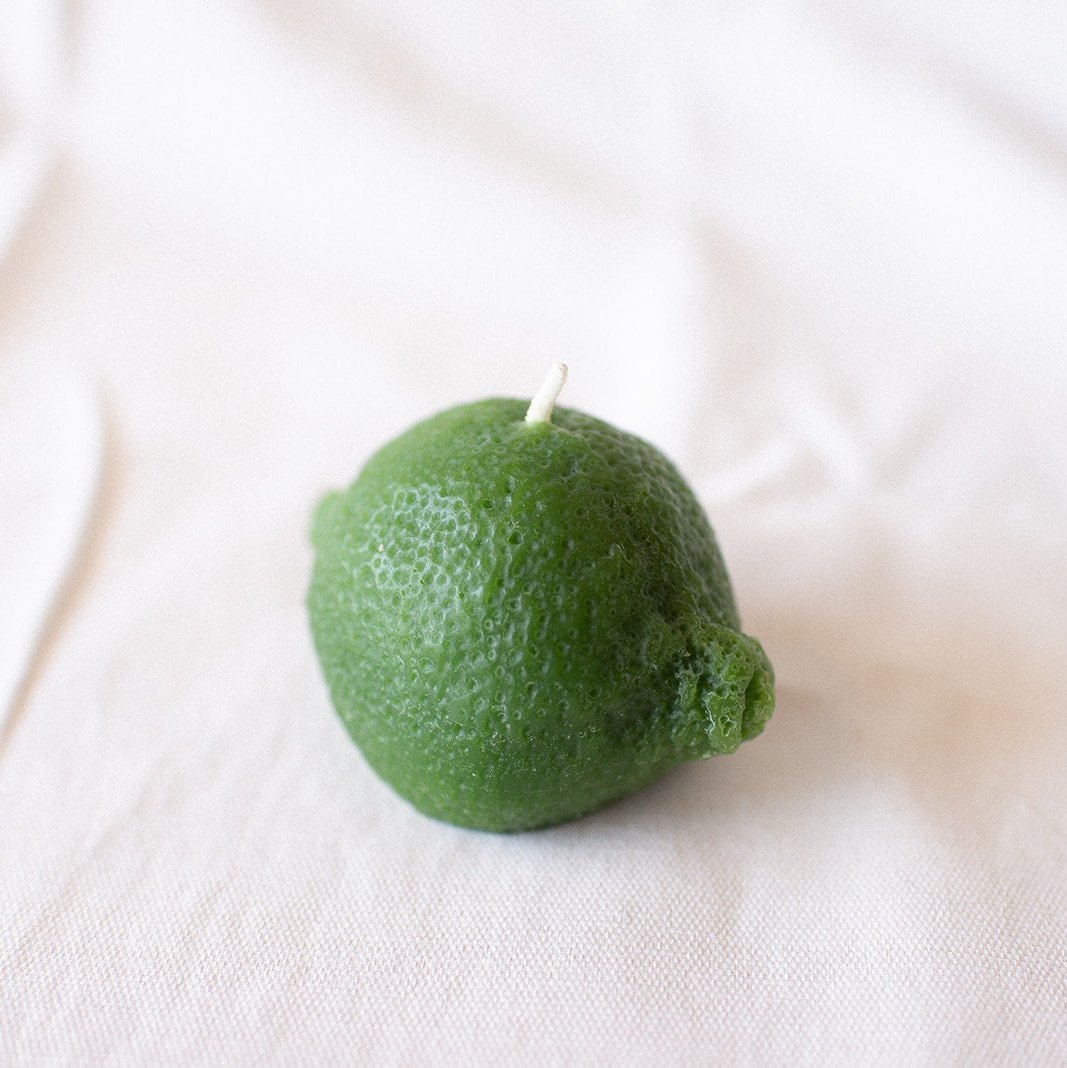 Green candle shaped like a lime on a white fabric background