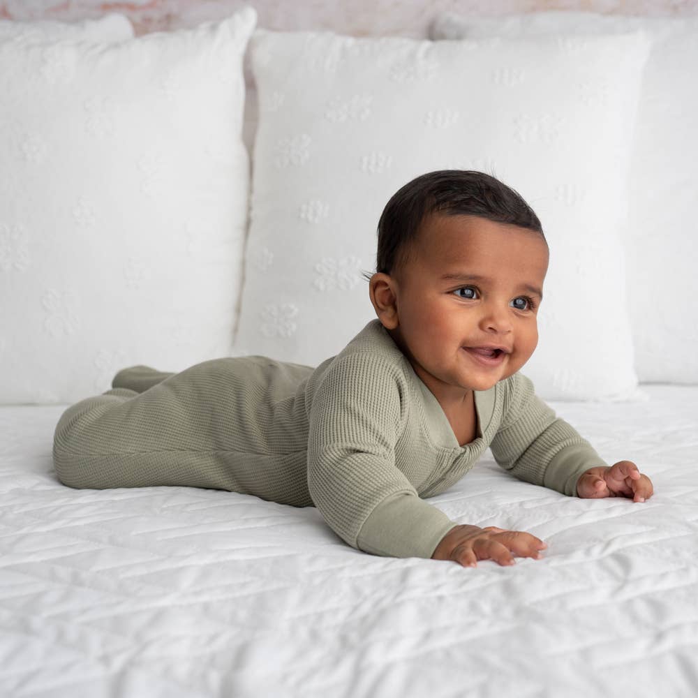 a baby laying on their stomach on a bed wearing olive organic zip foote