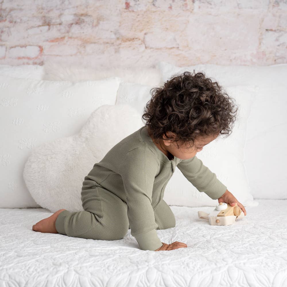 baby crawling on a bed wearing olive organic romper