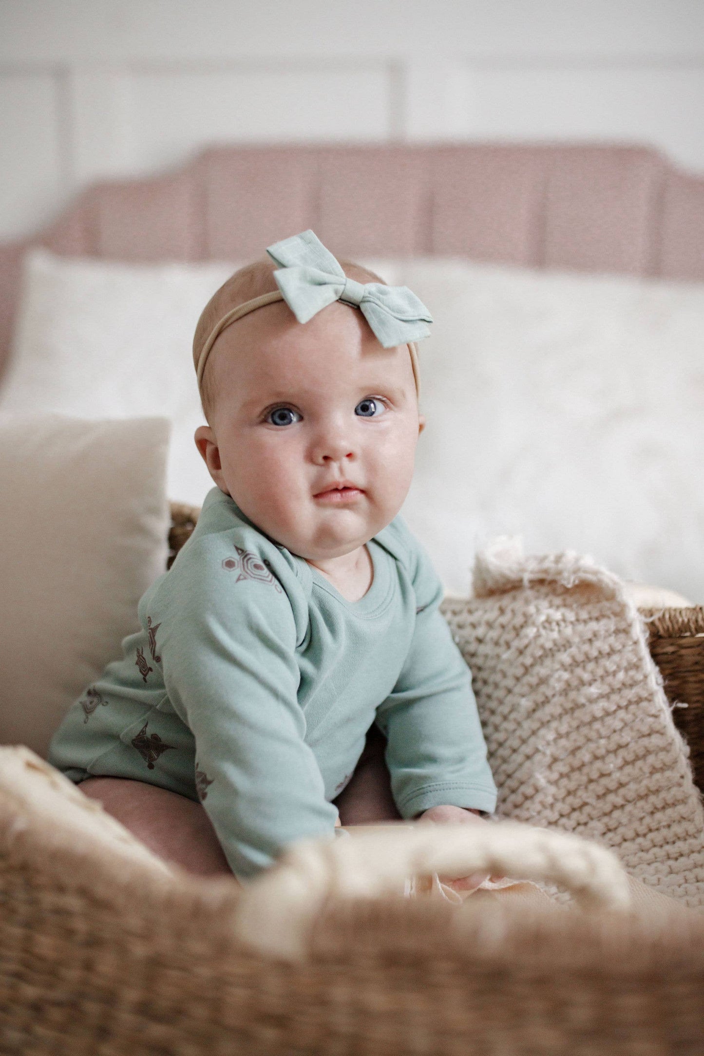 baby sitting in a crib wearing a bow and a long sleeve turtle print onesie