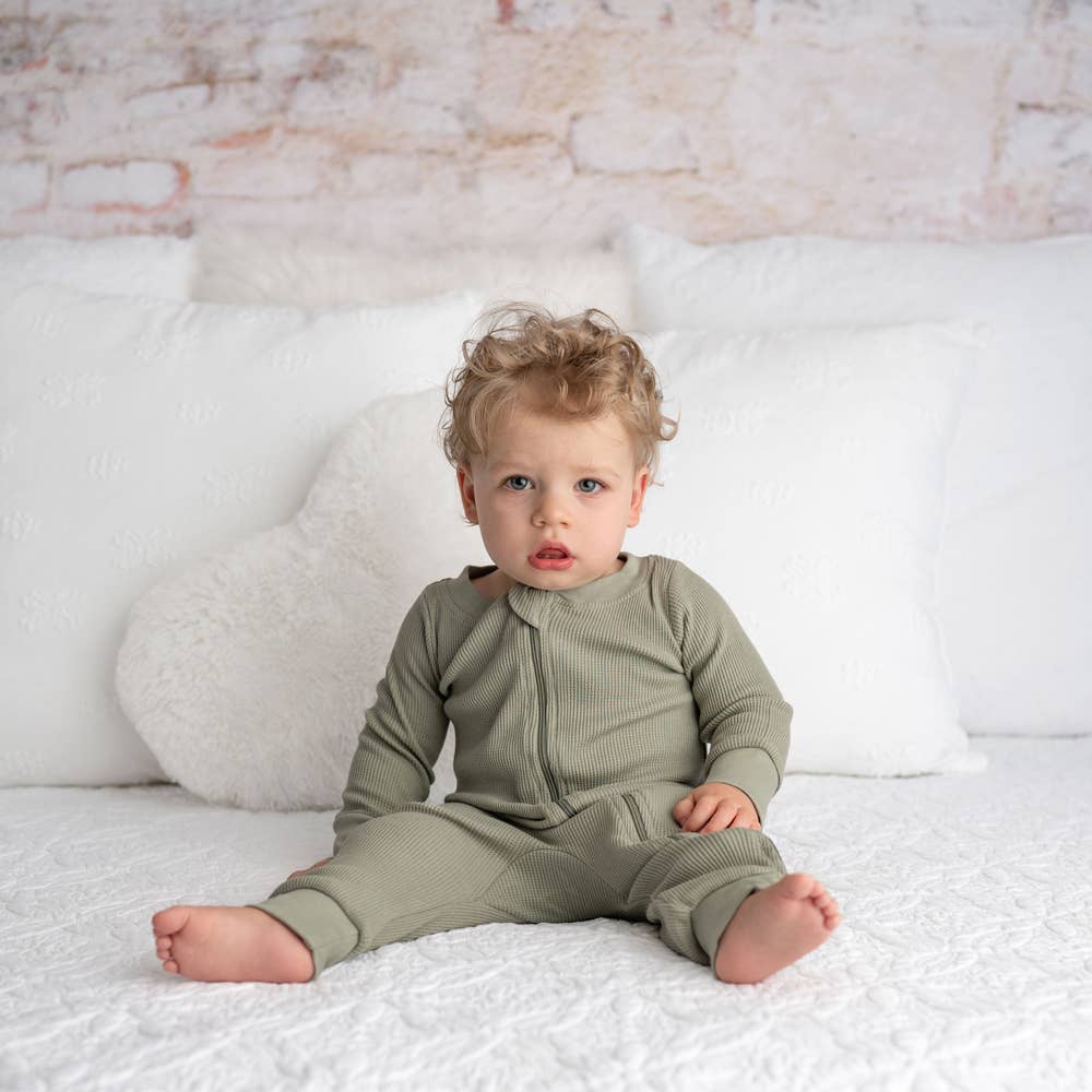 baby sitting on a bed wearing rganic olive waffle romper