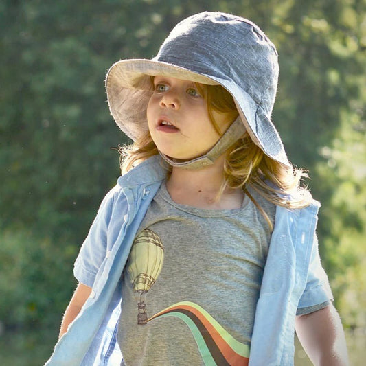 Child wearing a sun hat and light shirt with a hot air balloon design outdoors.