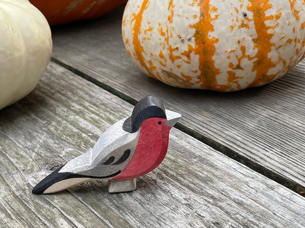 1 red bullfinch hand carved hand painted finch by ostheimer toys on a weathered wood with striped pumpkins int he back ground