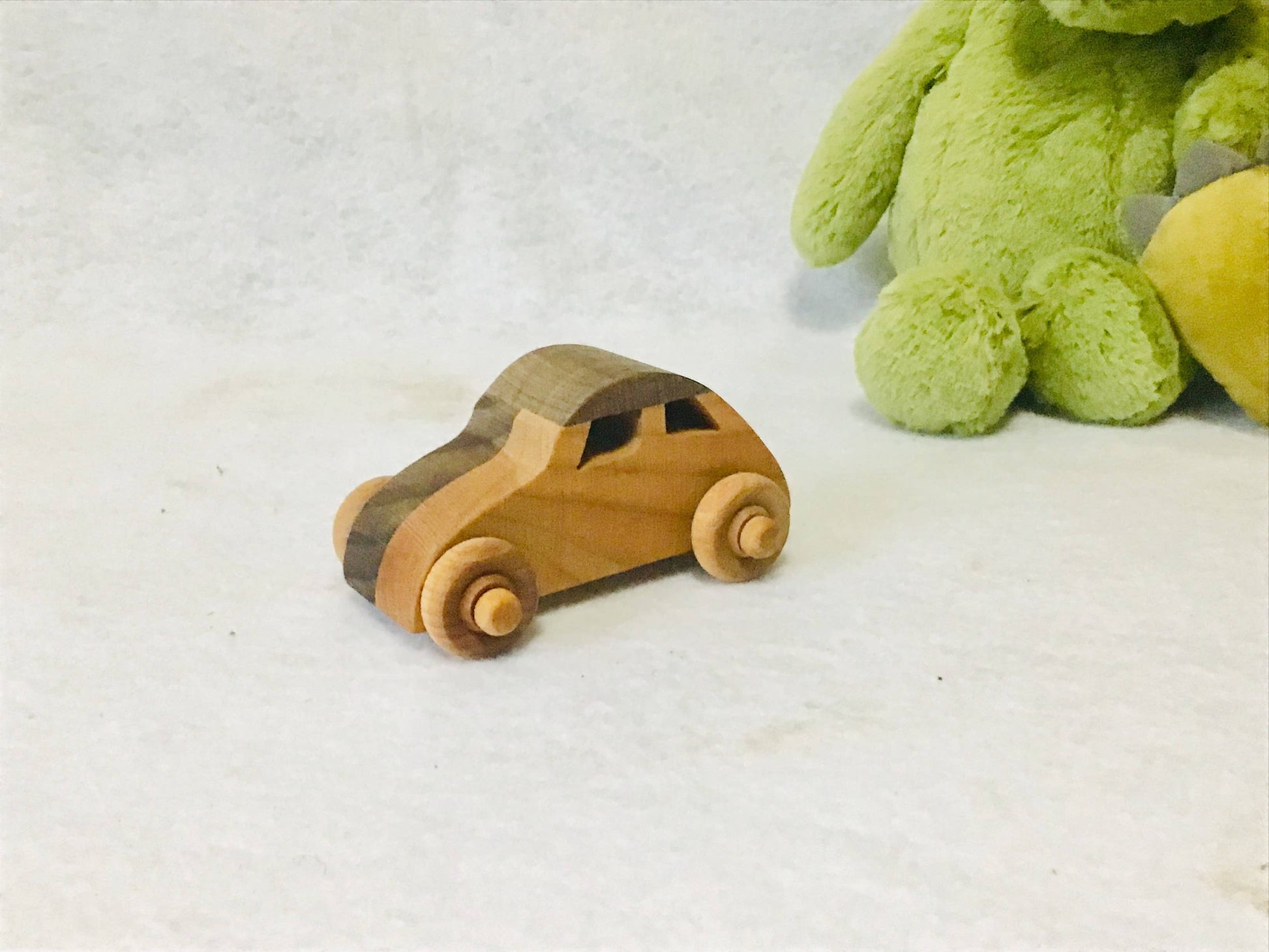 Wooden toy bug car next to a green plush toy on a light background