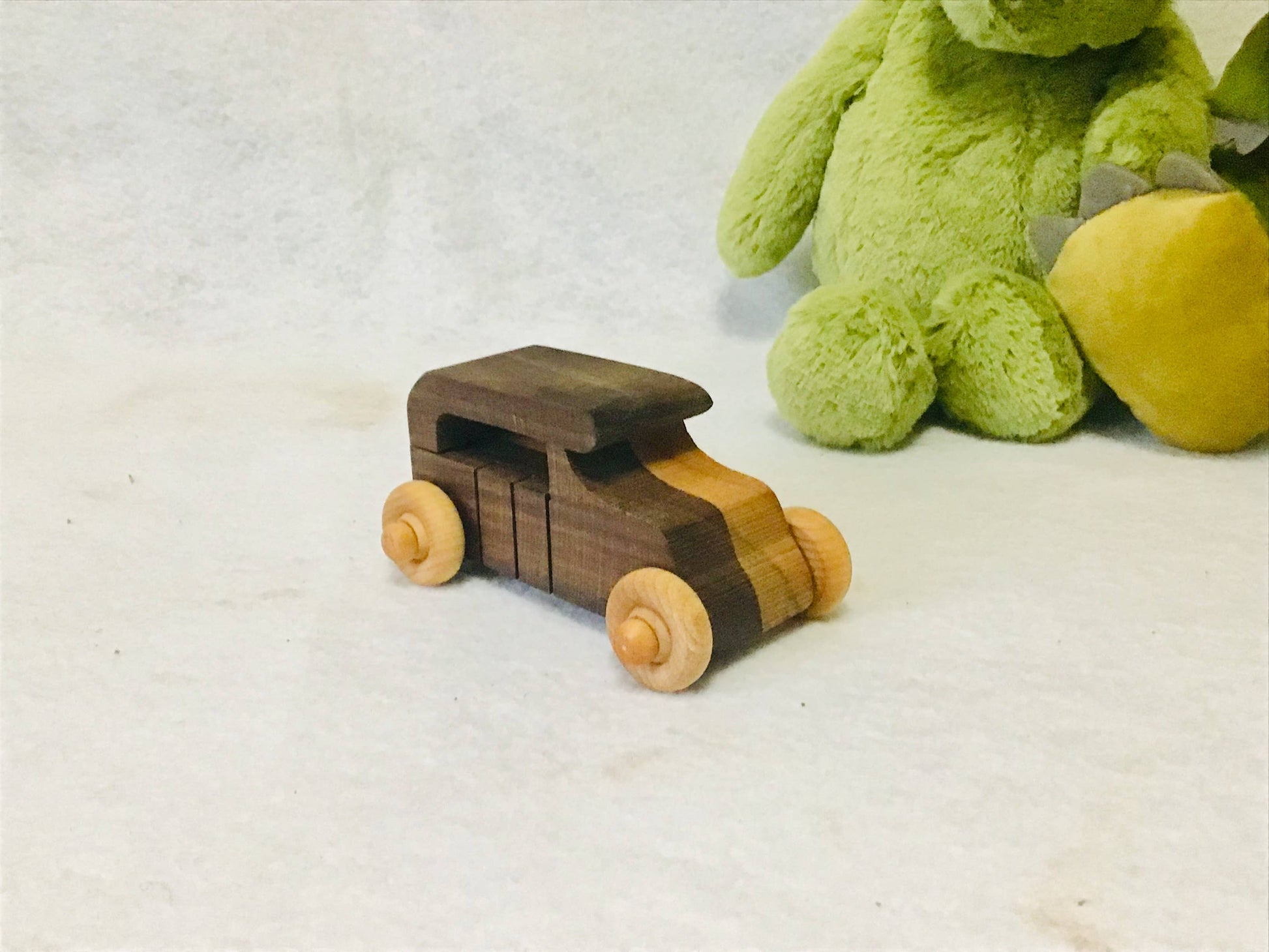 Wooden toy bus with wooden wheels on a white surface, next to a green plush toy.