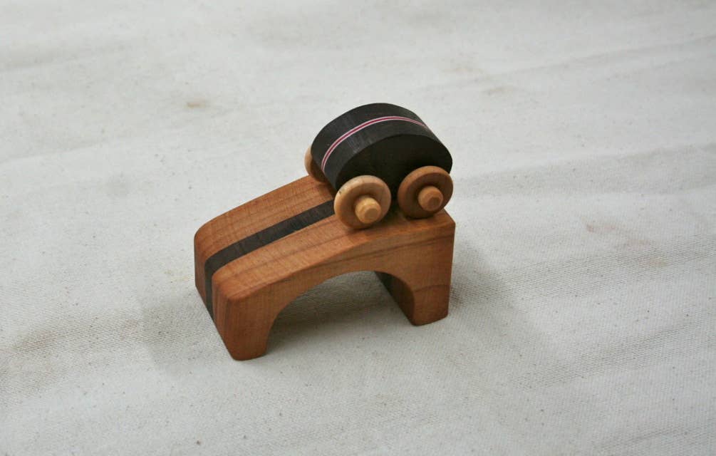 Wooden black toy car on a wooden ramp on a light gray background