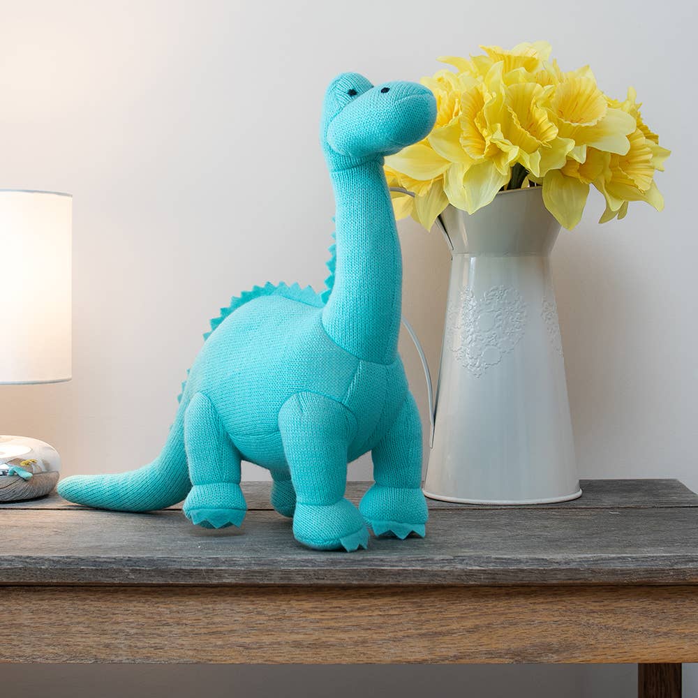 ice blue knitted diplodocus on a desk next to a flower vase