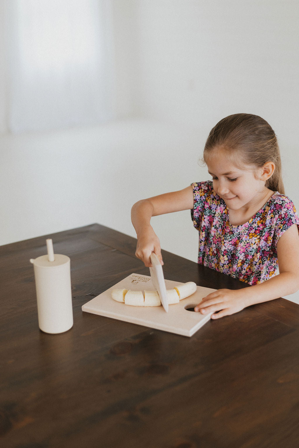 Young girl cutting cheese on a wooden board with a knife at a table.