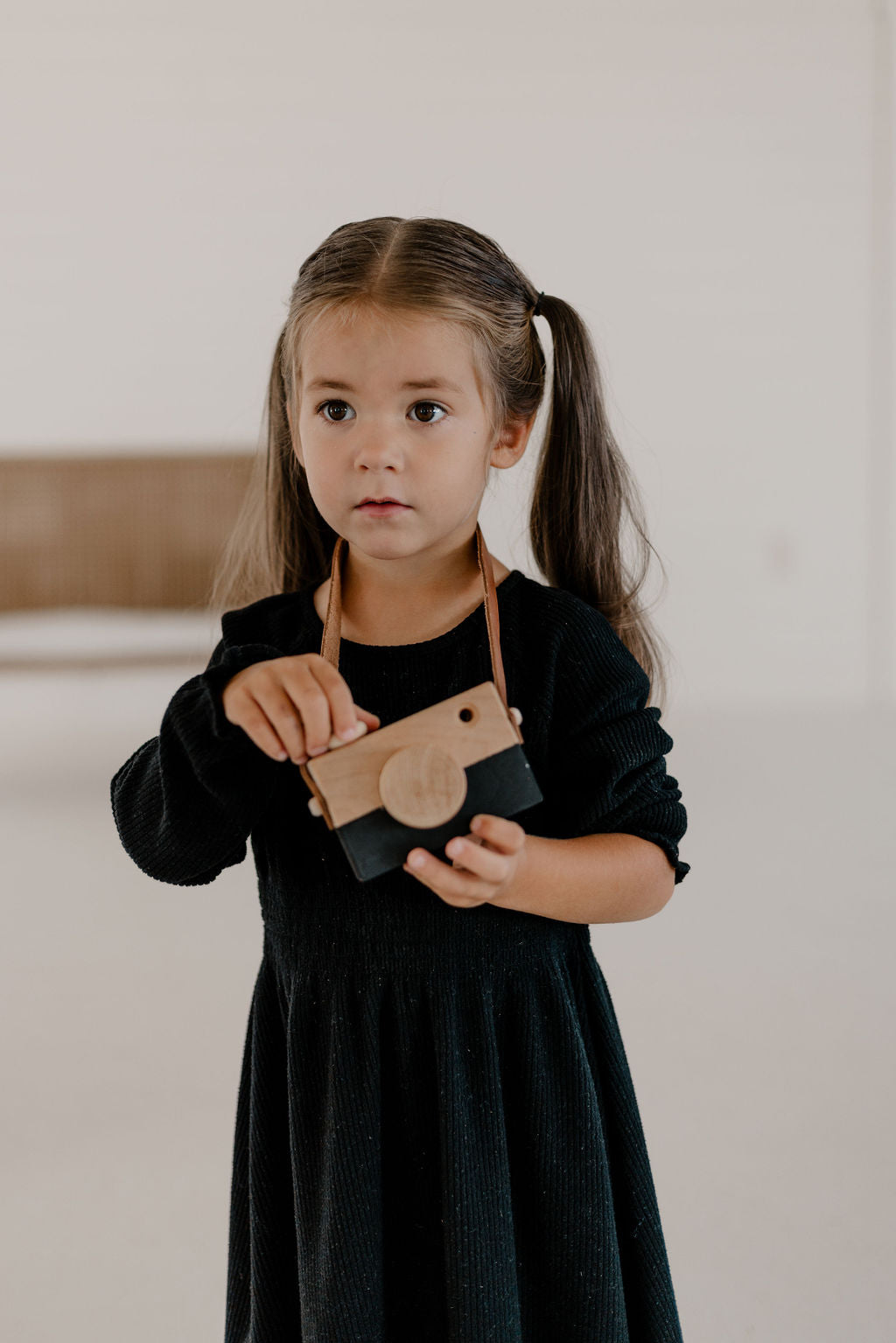 Young girl holding a wooden toy camera against a neutral background