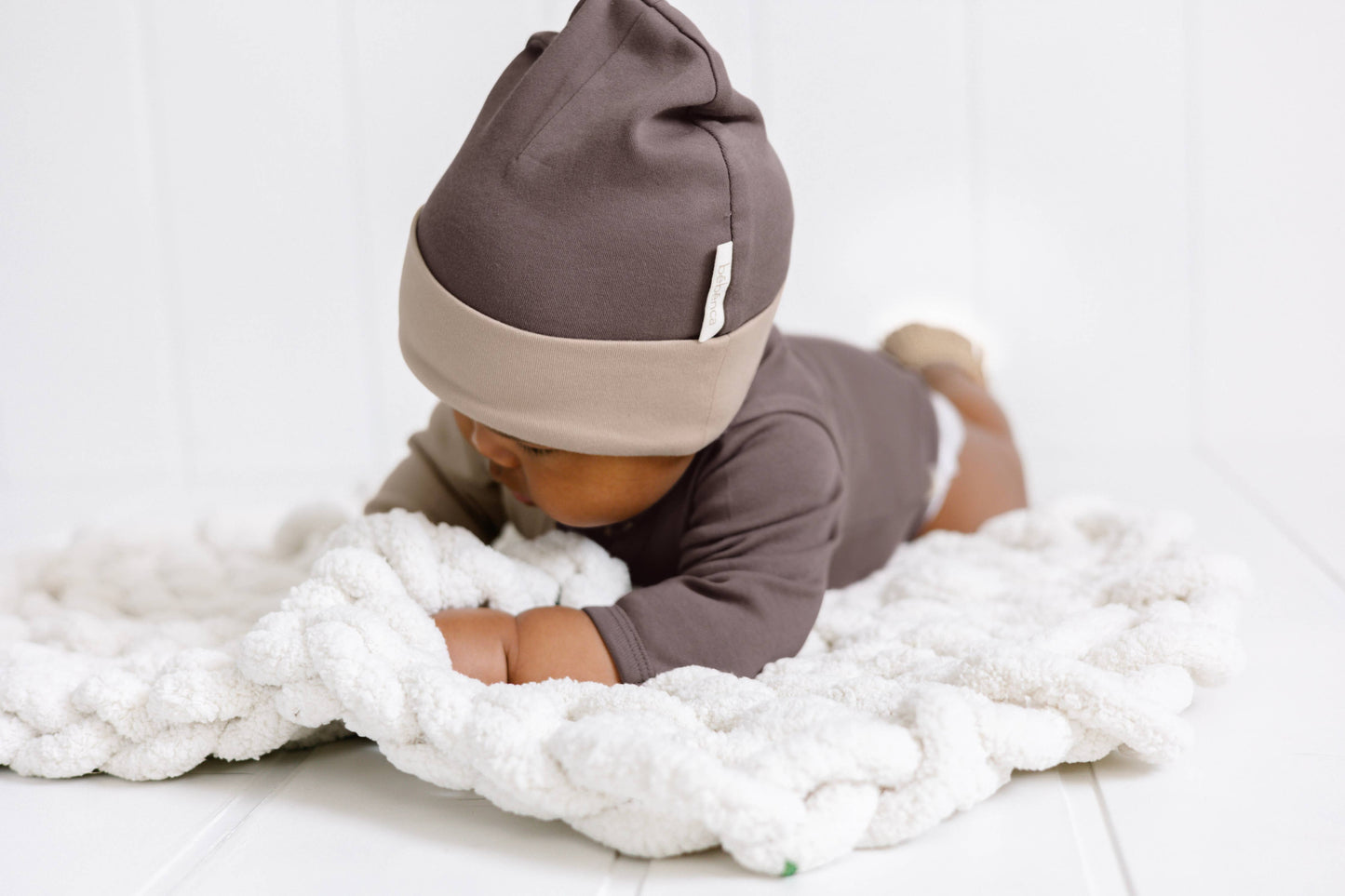 baby laying on their stomach on a blanket wearing aloha organic beanie