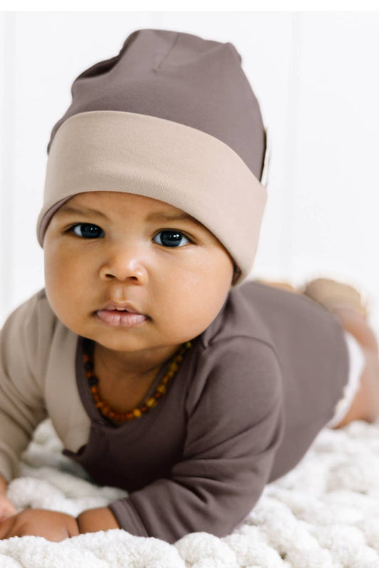 baby laying on their stomach on a bed wearing an aloha organic cotton beanie