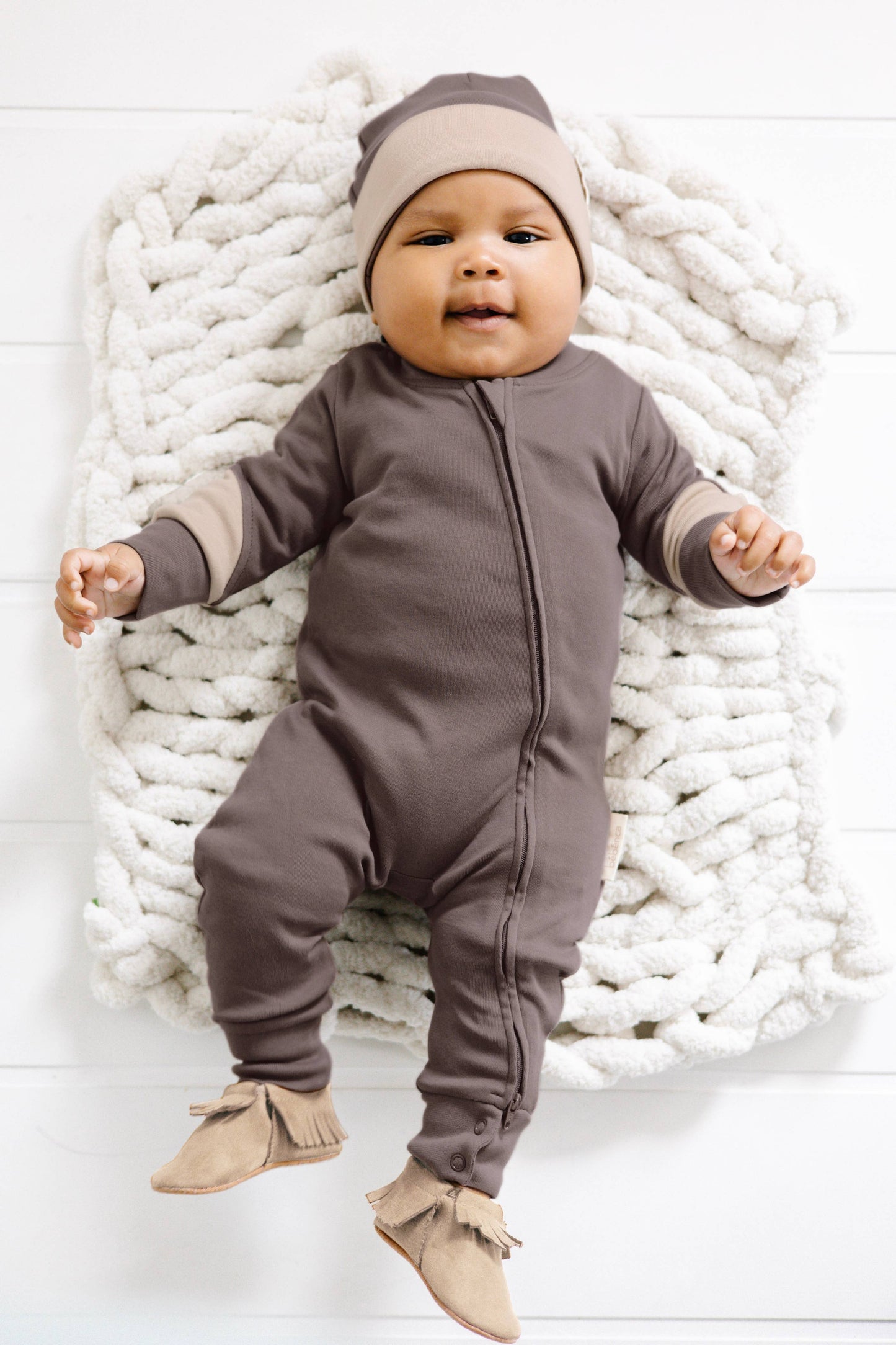 a baby laying on a blanket wearing matching brown romper and beanie