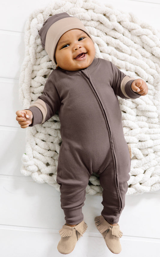 a baby laying on a blanket wearing matching brown romper and beanie