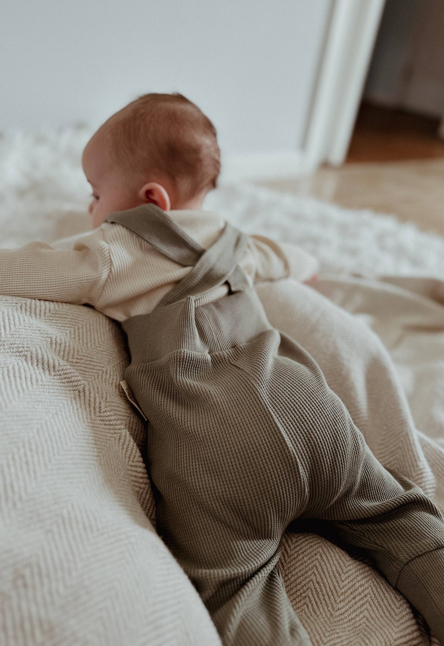 baby laying on their stomach on a bed wearing waffle tights with suspenders