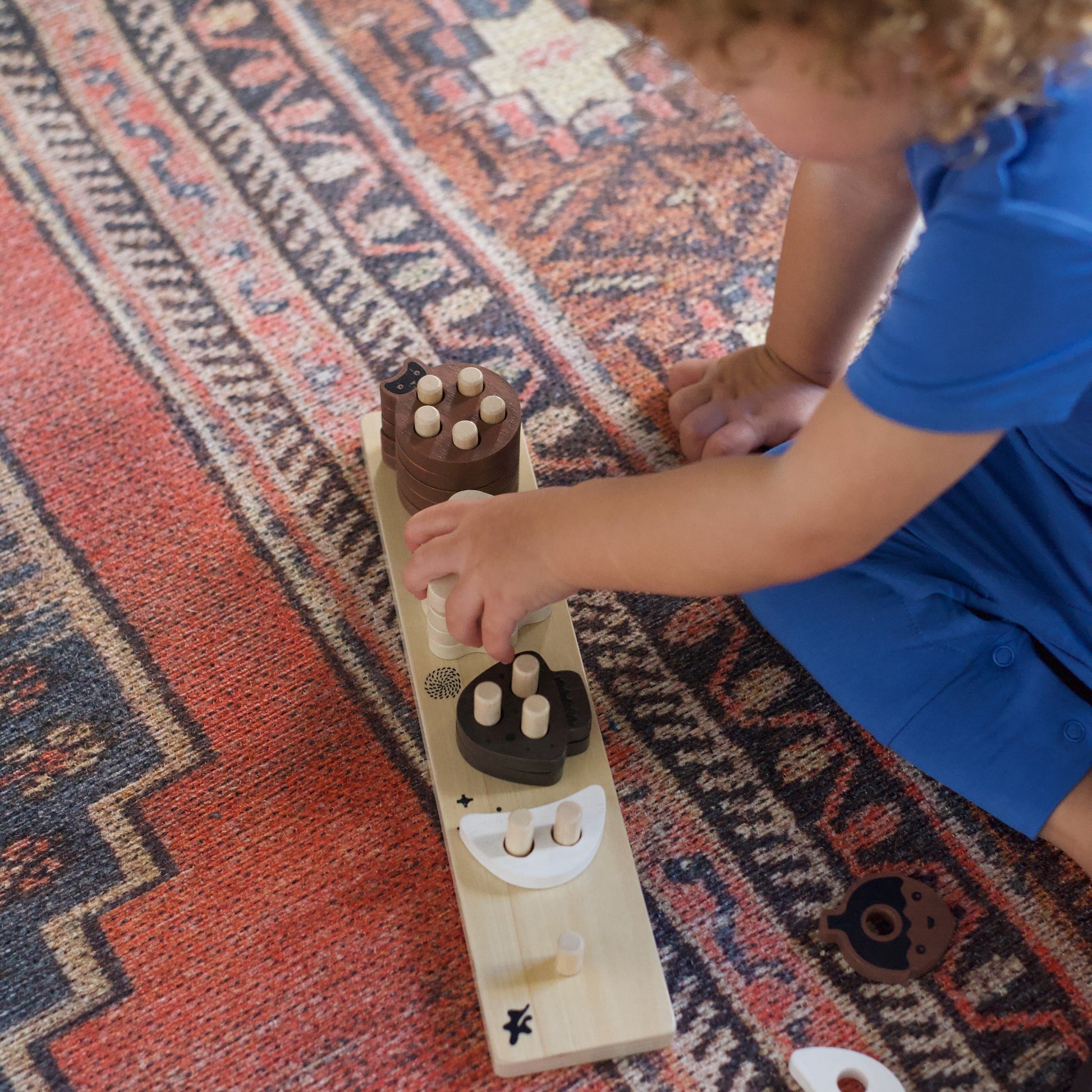 Child playing with a wooden puzzle on a patterned rug