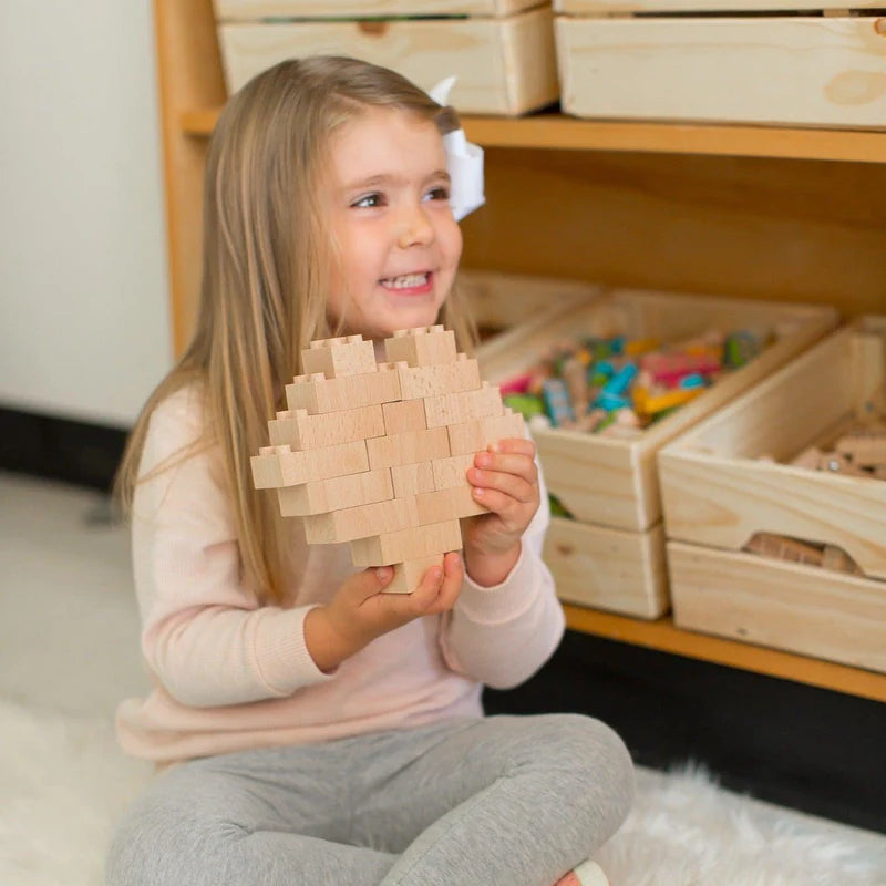 a toddler sitting on the floor holding a heart made of wooden Plus+ ecobricks