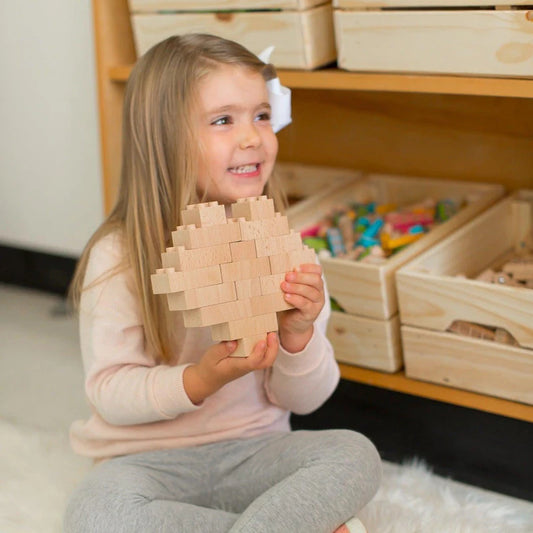 a toddler sitting on the floor holding a heart made of wooden Plus+ ecobricks