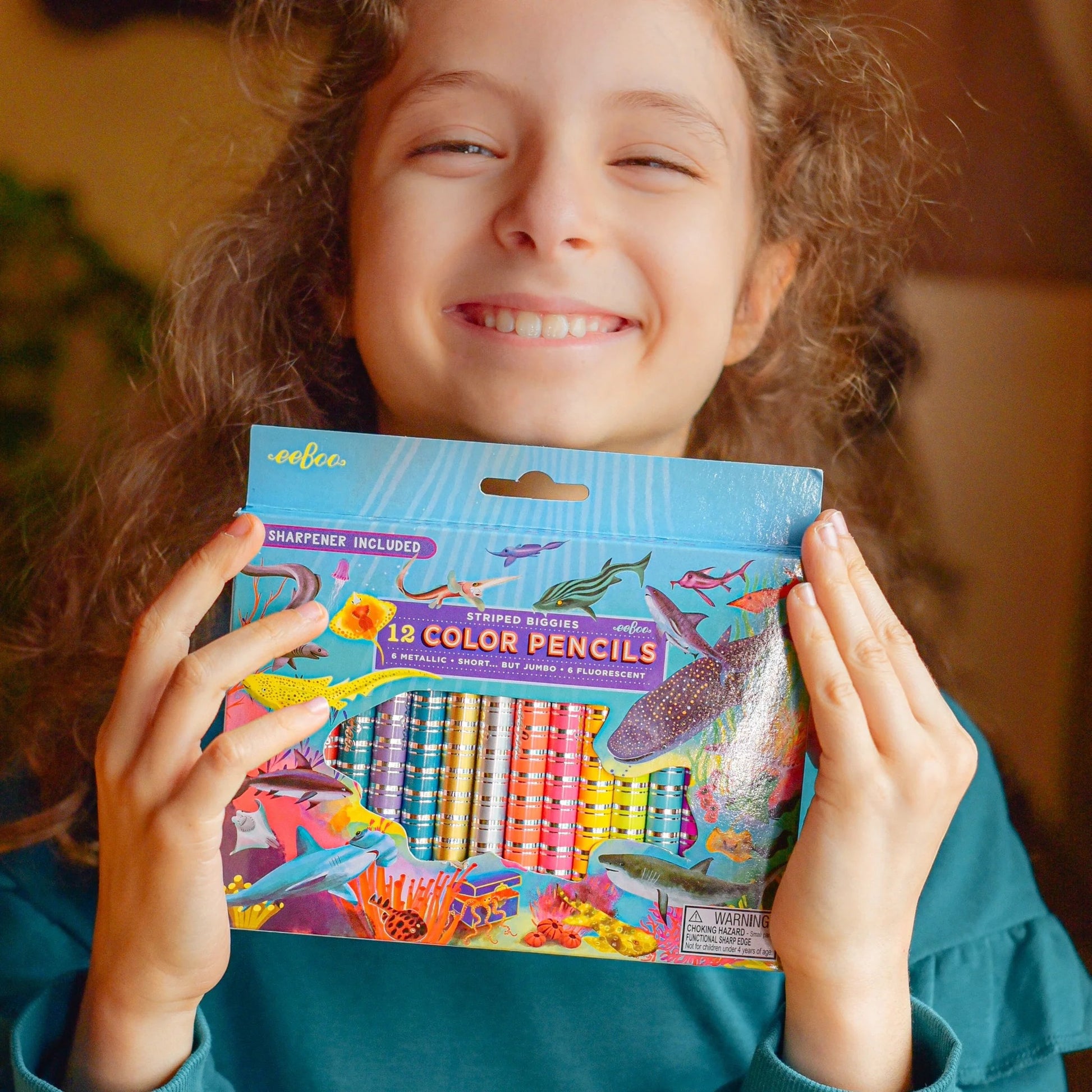 child wearing a blue sweater holding sharks biggie pencils while smiling