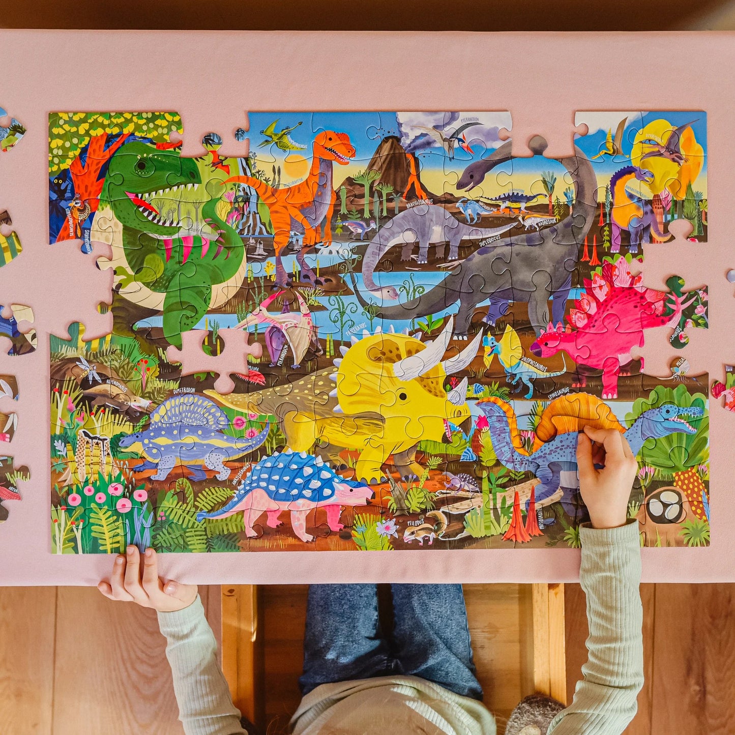 Child assembling a dinosaur-themed puzzle with colorful illustrations on a pink table.