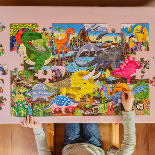 Child assembling a dinosaur-themed puzzle with colorful illustrations on a pink table.