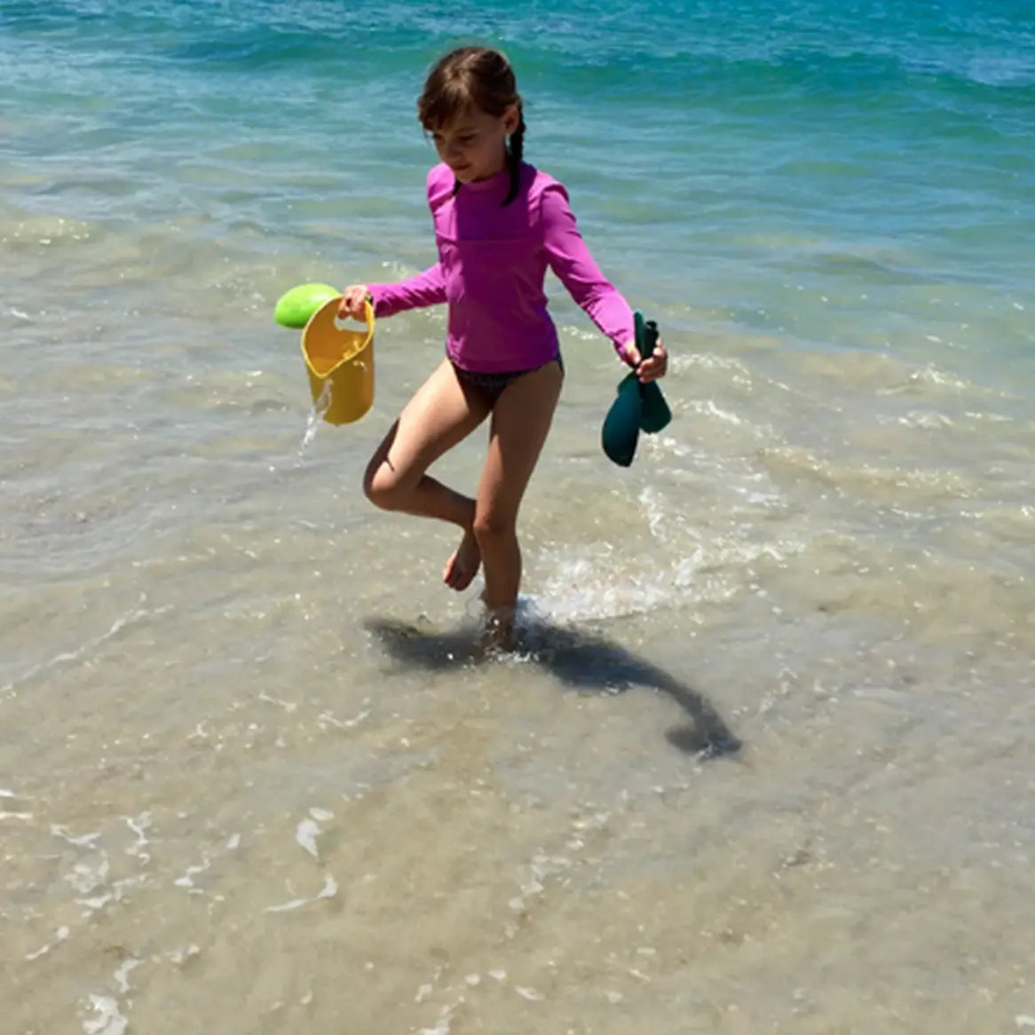 Child walking in the water holding bamboo sand bucket and play set